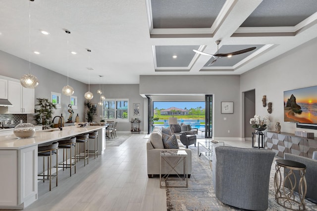 living room with ceiling fan, a textured ceiling, light hardwood / wood-style floors, crown molding, and coffered ceiling