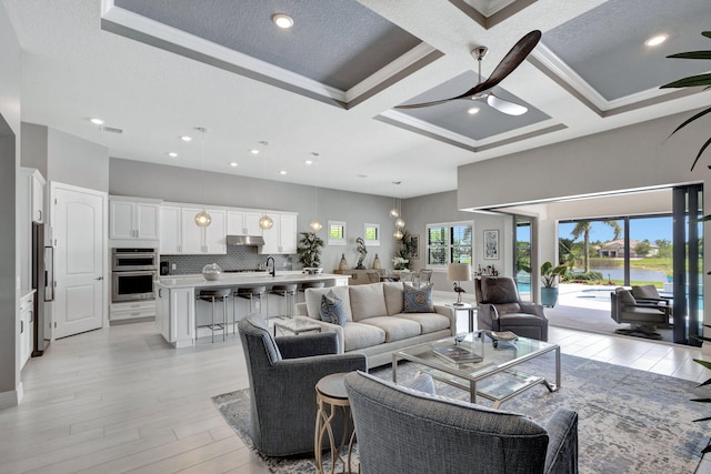 living room featuring a textured ceiling, light hardwood / wood-style floors, crown molding, sink, and coffered ceiling