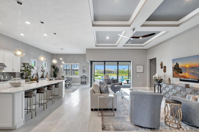 living room with coffered ceiling, beam ceiling, light hardwood / wood-style flooring, ornamental molding, and sink