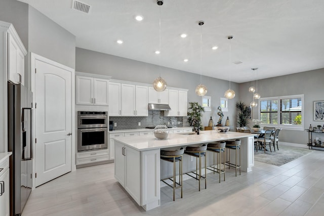 kitchen with a center island with sink, white cabinetry, stainless steel appliances, sink, and decorative light fixtures