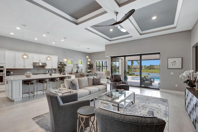 living room with ceiling fan, coffered ceiling, ornamental molding, and light wood-type flooring