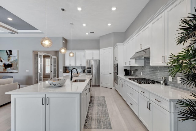 kitchen with appliances with stainless steel finishes, white cabinetry, a kitchen island with sink, sink, and decorative light fixtures