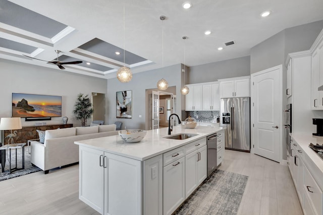 kitchen featuring appliances with stainless steel finishes, sink, hanging light fixtures, white cabinetry, and a center island with sink