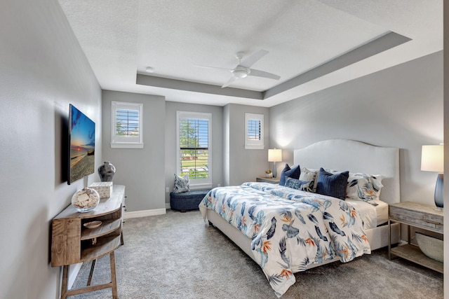 carpeted bedroom featuring a textured ceiling, a tray ceiling, and ceiling fan