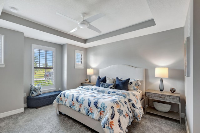 bedroom featuring carpet, a tray ceiling, a textured ceiling, and ceiling fan