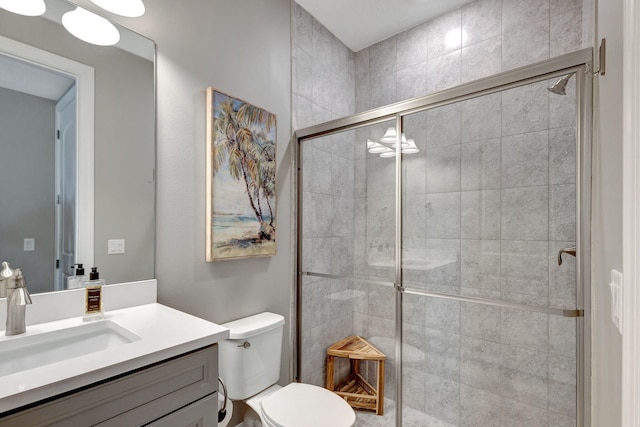 bathroom featuring toilet, a shower with shower door, and vanity