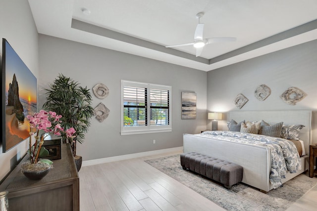 bedroom with a tray ceiling, light wood-type flooring, and ceiling fan