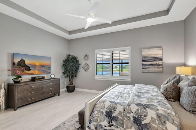 bedroom with ceiling fan, a tray ceiling, and light hardwood / wood-style floors