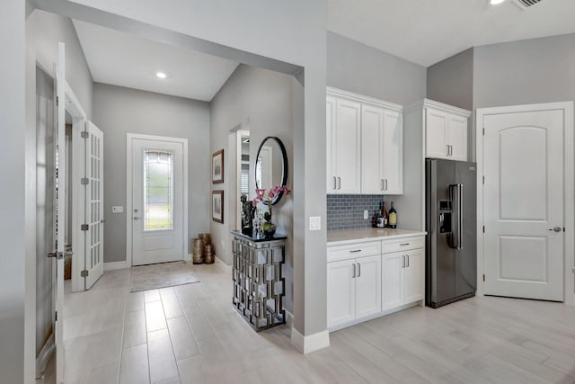 kitchen featuring high end refrigerator, white cabinets, light hardwood / wood-style floors, and tasteful backsplash