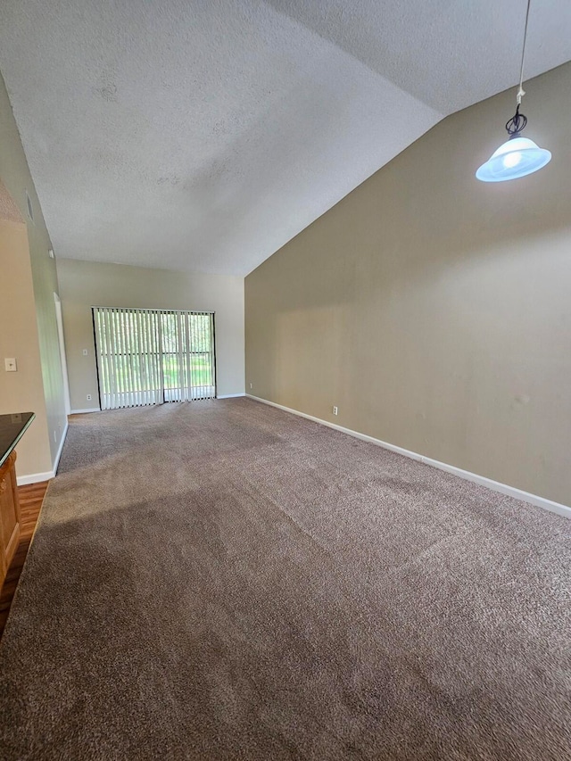 spare room featuring lofted ceiling, dark colored carpet, and a textured ceiling