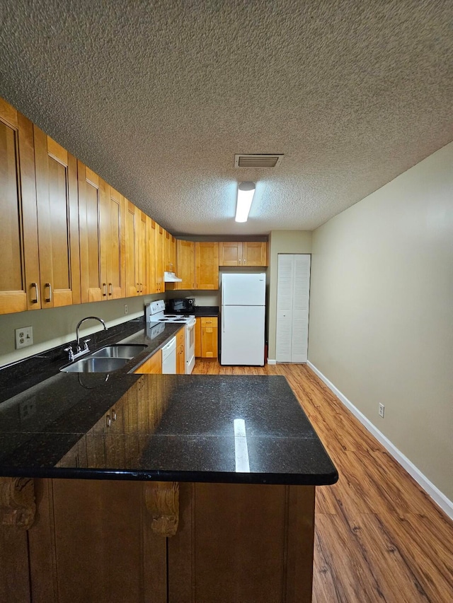 kitchen featuring hardwood / wood-style flooring, kitchen peninsula, sink, a textured ceiling, and white appliances