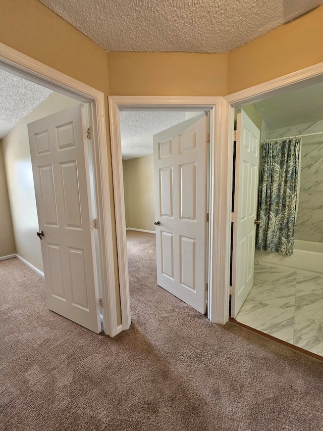 hallway with a textured ceiling and light colored carpet