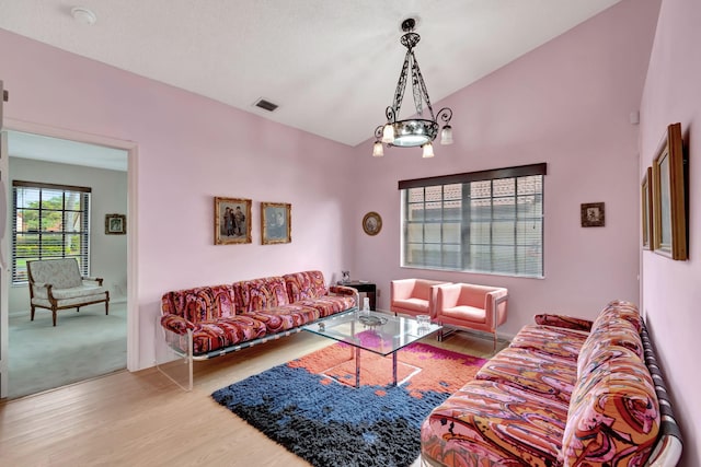 living room with lofted ceiling, wood-type flooring, and an inviting chandelier