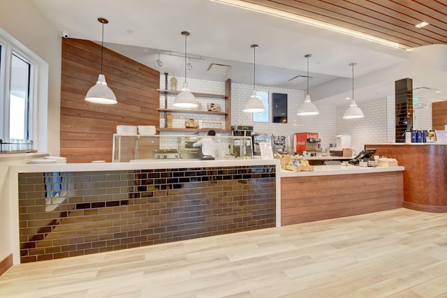 kitchen featuring wood walls, light hardwood / wood-style flooring, pendant lighting, and brick wall