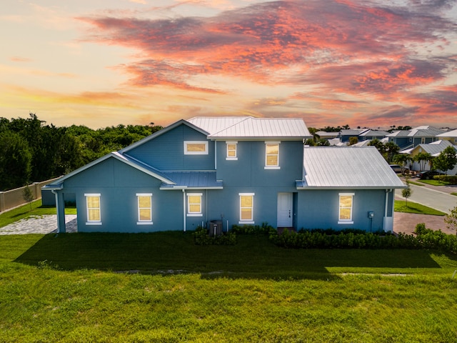 back house at dusk featuring central AC unit and a lawn