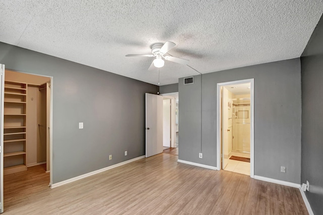 unfurnished bedroom with connected bathroom, a closet, light wood-type flooring, ceiling fan, and a spacious closet