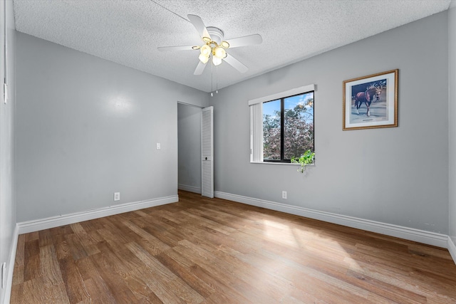 empty room with ceiling fan, light wood-type flooring, and a textured ceiling