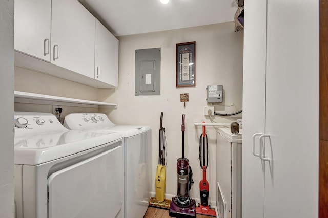 washroom featuring electric panel, washing machine and dryer, cabinets, and wood-type flooring