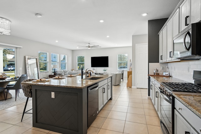 kitchen with sink, appliances with stainless steel finishes, light stone countertops, an island with sink, and white cabinets