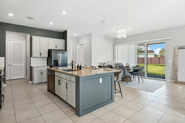 kitchen with a center island with sink, light tile patterned floors, light stone countertops, stainless steel refrigerator with ice dispenser, and sink