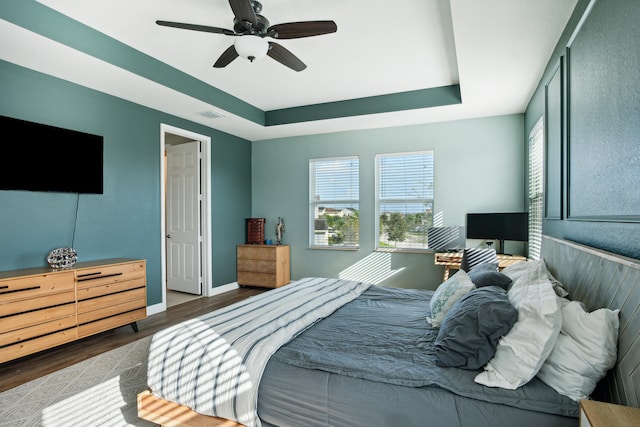 bedroom with dark wood-type flooring, ceiling fan, and a raised ceiling