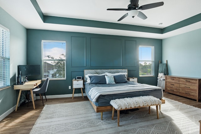 bedroom with a tray ceiling, multiple windows, hardwood / wood-style floors, and ceiling fan