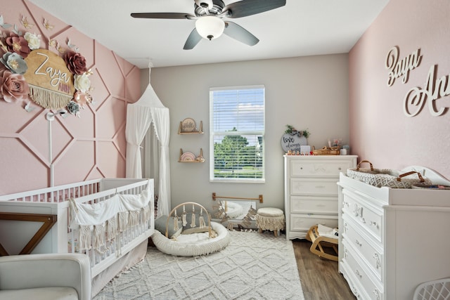 bedroom with hardwood / wood-style floors, a crib, and ceiling fan