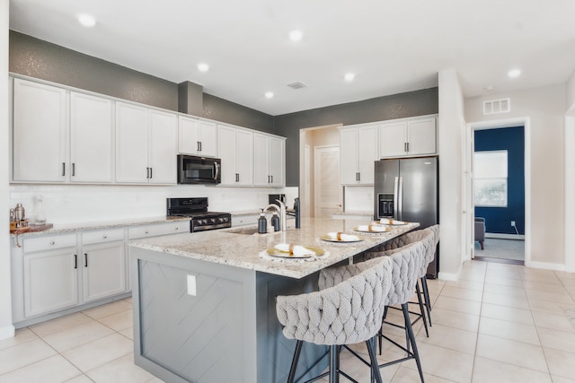 kitchen featuring sink, black appliances, light tile patterned floors, an island with sink, and white cabinets