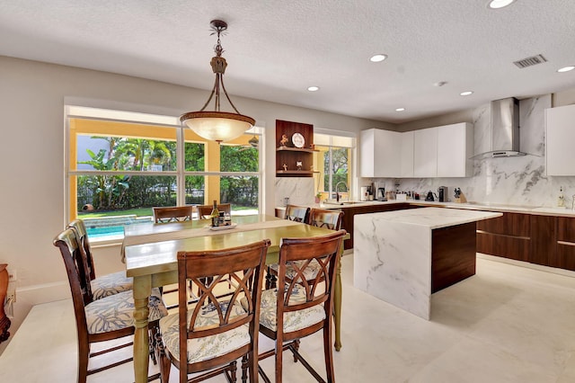 kitchen featuring a kitchen island, wall chimney range hood, dark brown cabinetry, decorative light fixtures, and white cabinets