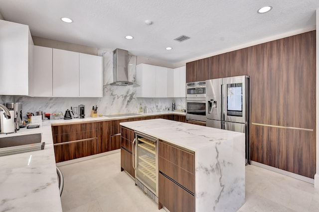 kitchen featuring light stone countertops, wall chimney range hood, backsplash, and white cabinets