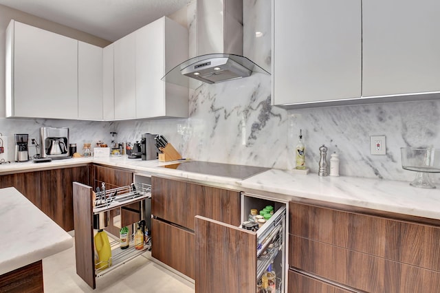 kitchen with wall chimney exhaust hood, decorative backsplash, white cabinetry, light stone countertops, and black electric stovetop