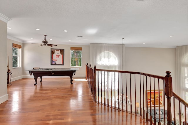 corridor with light hardwood / wood-style floors, a textured ceiling, ornamental molding, and a wealth of natural light