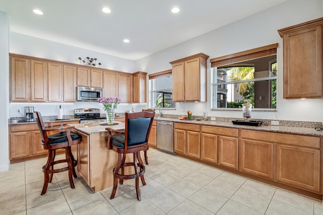 kitchen with a center island, a kitchen breakfast bar, light stone counters, light tile patterned flooring, and appliances with stainless steel finishes