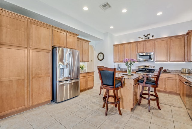 kitchen with a center island, a kitchen breakfast bar, appliances with stainless steel finishes, light tile patterned flooring, and light stone counters