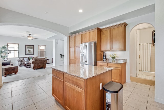 kitchen with ceiling fan, light tile patterned floors, a kitchen island, light stone counters, and stainless steel fridge with ice dispenser