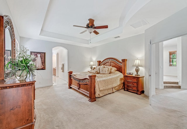 carpeted bedroom featuring ceiling fan, ensuite bathroom, and a tray ceiling