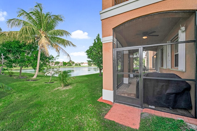 view of yard featuring a sunroom, ceiling fan, and a water view