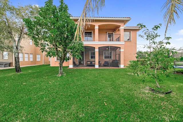 rear view of house with a balcony, ceiling fan, a patio area, and a lawn