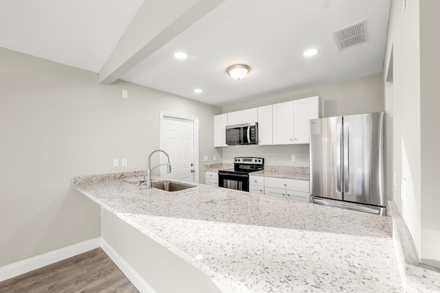 kitchen with kitchen peninsula, appliances with stainless steel finishes, white cabinets, light stone counters, and sink