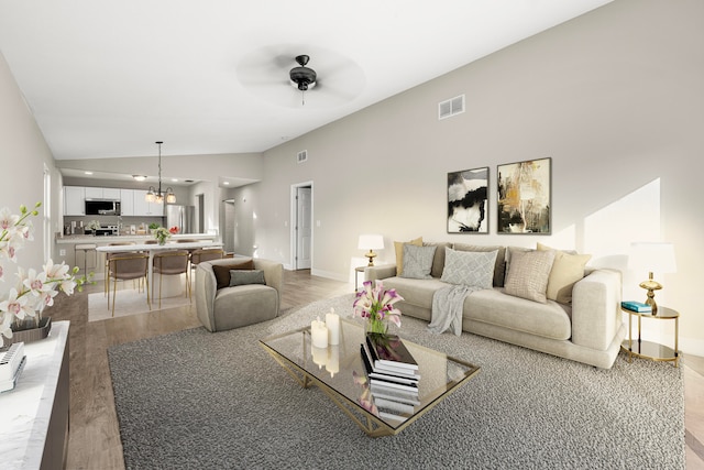 living room with ceiling fan with notable chandelier, light hardwood / wood-style flooring, and vaulted ceiling