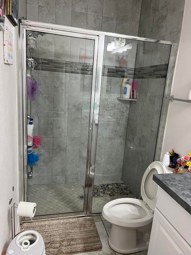 bathroom featuring a shower with door, vanity, toilet, and tile patterned flooring