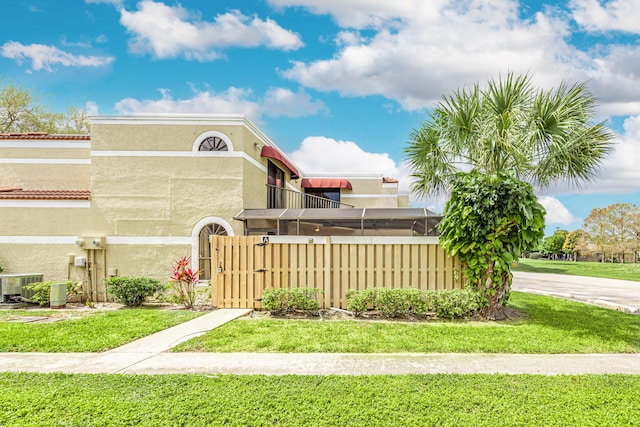 view of front of house featuring stucco siding, central AC unit, a front yard, a gate, and fence