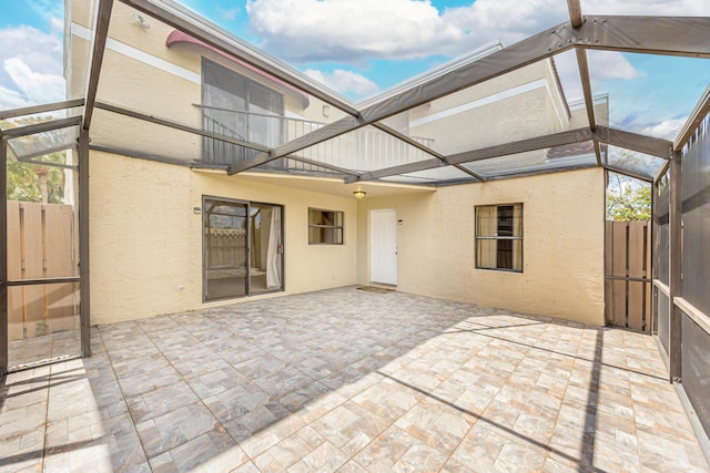 back of property with a patio area, glass enclosure, fence, and stucco siding