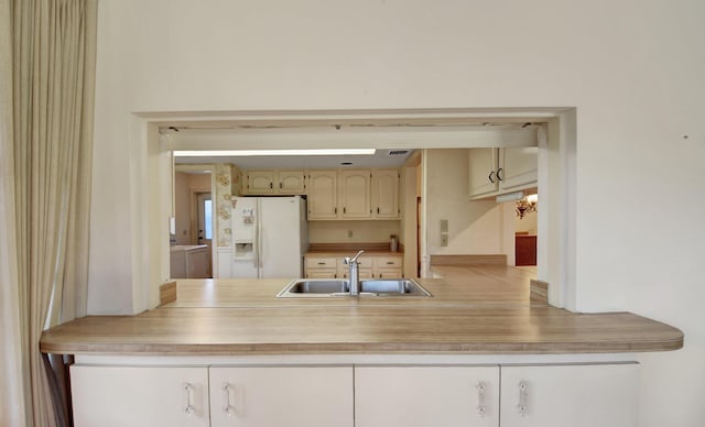 kitchen featuring white refrigerator with ice dispenser, cream cabinets, and sink