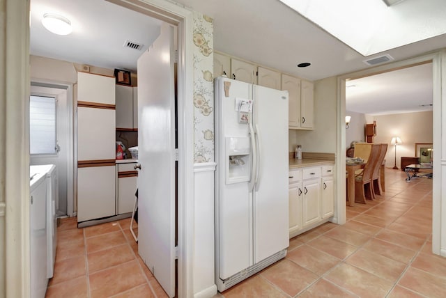 kitchen featuring white cabinets, washing machine and dryer, white refrigerator with ice dispenser, and light tile patterned floors