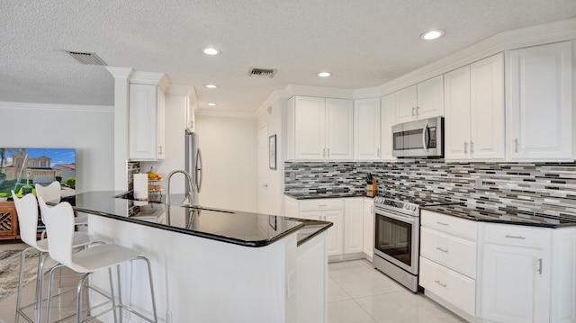 kitchen featuring sink, kitchen peninsula, light tile patterned floors, appliances with stainless steel finishes, and white cabinetry