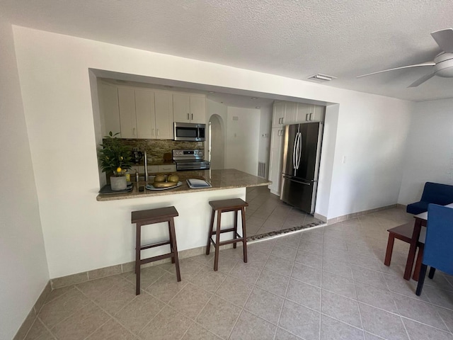 kitchen featuring decorative backsplash, a breakfast bar area, kitchen peninsula, stainless steel appliances, and ceiling fan