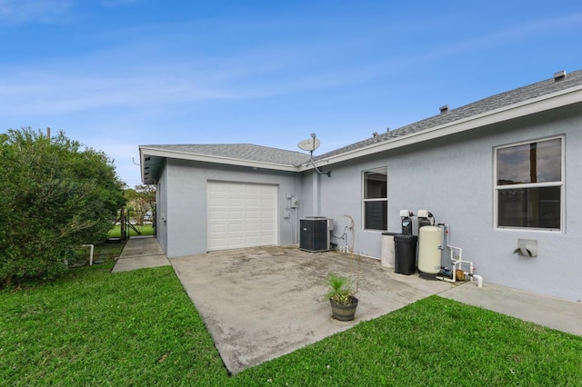 rear view of property with a garage, cooling unit, and a lawn