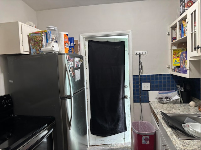 kitchen featuring sink, backsplash, black electric range oven, stainless steel fridge, and white cabinetry