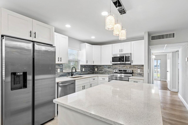 kitchen with light hardwood / wood-style flooring, stainless steel appliances, light stone countertops, pendant lighting, and white cabinetry